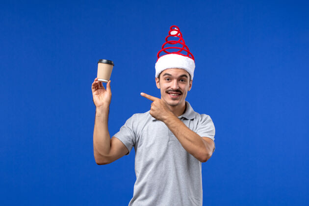 风景正面图年轻男子拿着塑料咖啡杯站在蓝色的墙上过年男子过节前面圣诞节举行