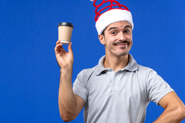 专业正面图年轻男性手持塑料咖啡杯在蓝色背景上除夕夜男性放假年轻男性人男性