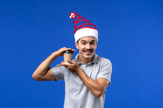 举行正面图年轻男性手持塑料咖啡杯在蓝色墙壁上新年男性假期成人运动男