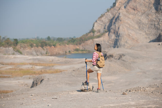 运动适合年轻女子徒步在山上站在岩石山顶山脊与背包和杆眺望风景岩石旅行女性