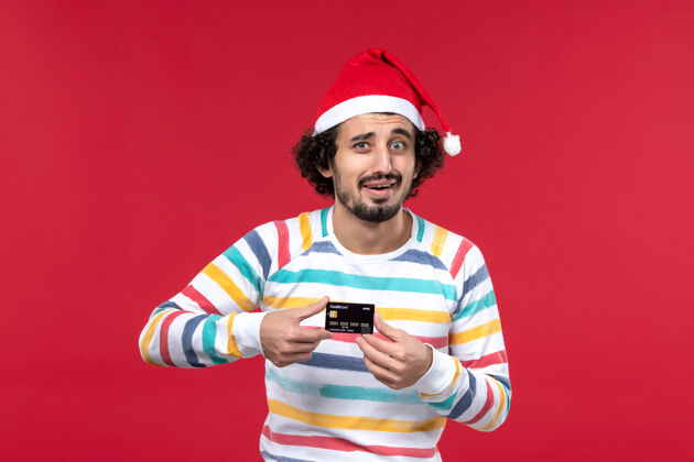 男正面图年轻男子拿着银行卡在淡红色的墙上男红色的节日情感男圣诞节表演