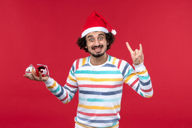 视图正面图年轻人拿着圣诞树玩具在红墙新年红人节微笑人前面
