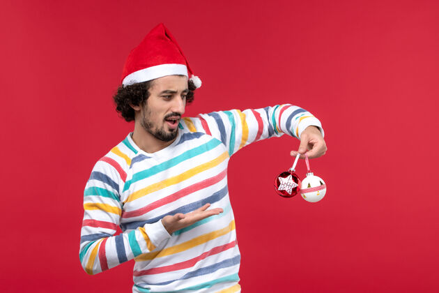 圣诞节正面图红墙上拿着塑料玩具的年轻人人类节日新年红帅哥年轻人娱乐