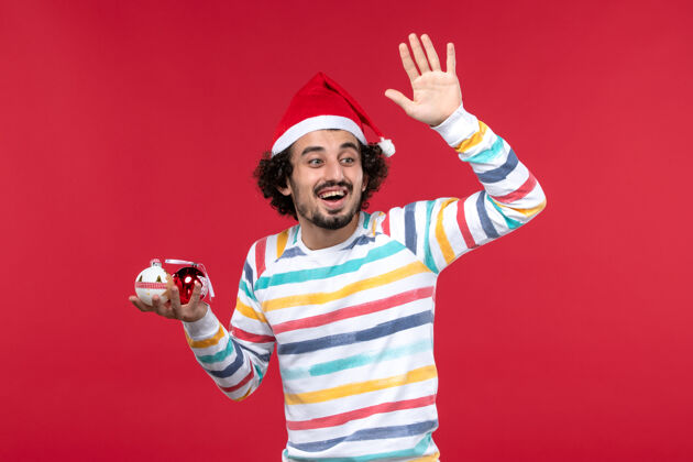 看面图年轻人拿着圣诞树玩具在红墙假日红人新年玩具前面球员