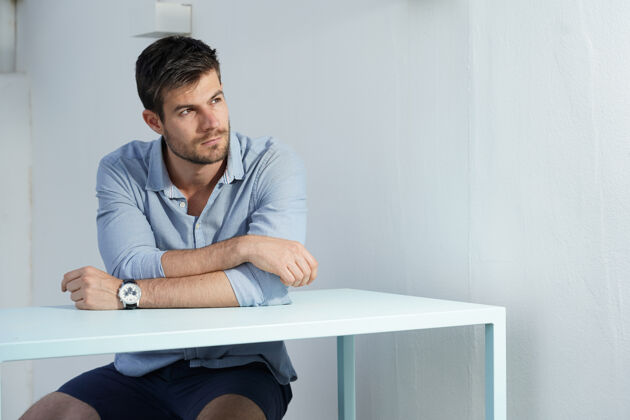 技术穿着蓝色衬衫的年轻西班牙裔男子在一张白色书桌旁摆姿势专业人员办公室