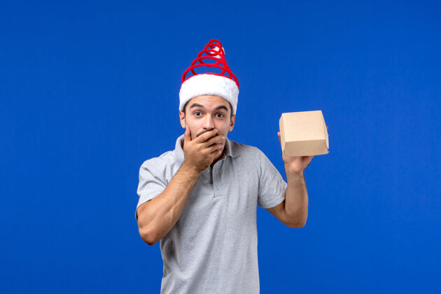 圣诞节正面图年轻男子拿着食品包在蓝色墙上的餐饮服务工作工作正面举行
