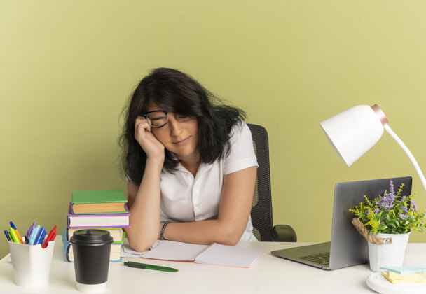 疲惫年轻疲惫漂亮的白人女学生戴着眼镜坐在书桌旁 手放在脸上 在绿色空间和复印空间上睡觉女学生眼镜穿