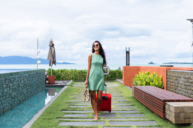 旅游快乐的白种人漂亮的长发优雅的旅游女人在酒店外面穿着红色的手提箱孤独度假行李