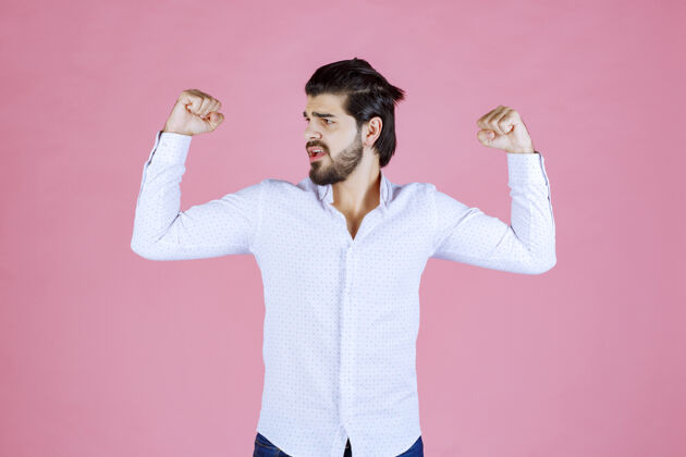 成人一个穿白衬衫的男人在展示他的手臂肌肉聪明强壮健康