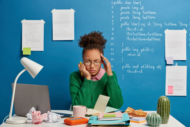 疲倦压力大的学生感到身体不适 头晕头痛 不能工作 在记事本上写下要做的事情 在蓝色背景下摆姿势 写下信息非洲裔桌子精疲力尽