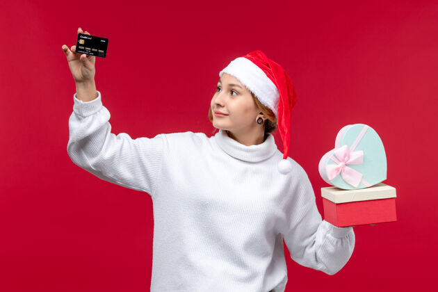 视图前视图年轻女子手持礼物和银行卡在红色背景上微笑成人帽子
