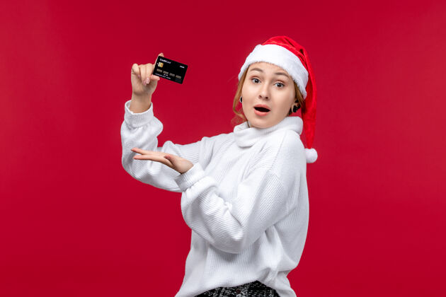 帽子正面图年轻女子拿着银行卡站在红色的地板上红色的圣诞钱微笑肖像童年