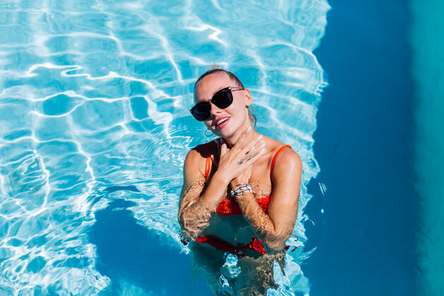 女孩阳光明媚的日子里 蓝色游泳池里 戴着太阳镜 皮肤黝黑的平静快乐女人的画像放松西装优雅