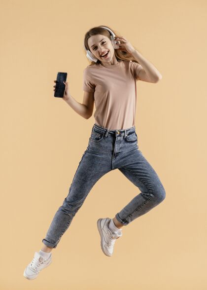 跳跃带着耳机和手机跳跃的年轻女性耳机模特表达