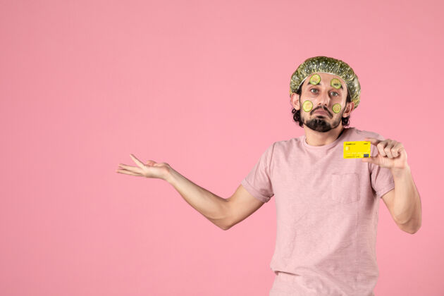 自我护理正面图：戴着面具的年轻男子 手持粉色背景的银行卡年轻男性肖像正面