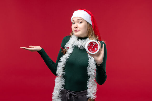 服装正面图红色背景上手持时钟的年轻女性举行肖像圣诞节