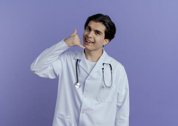 电话令人印象深刻的年轻男医生穿着医用长袍和听诊器做呼叫手势隔离在紫色的墙上与复制空间男性印象听诊器