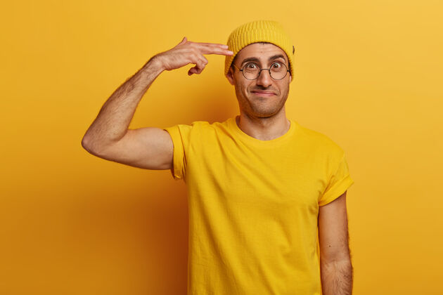 白种人沮丧的成年男性展示 手指靠近太阳穴 皱着眉头 心疼有很多工作要做 戴着黄色的帽子和t恤表情压力人