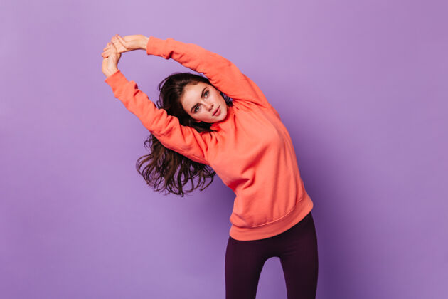 头紫色墙上卷曲的黑发女人做练习的画像连帽衫健身橙色裤子