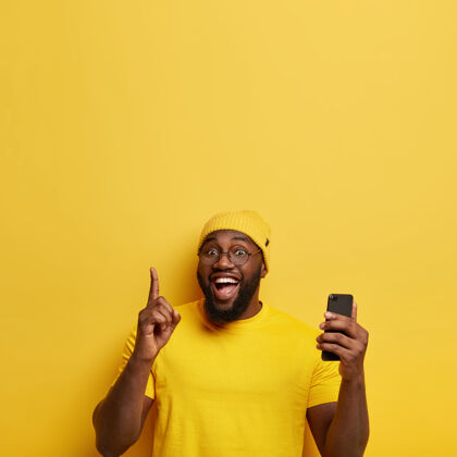 设备开朗的男人把食指指向上方 创建自己的博客 在智能手机上浏览社交媒体 有愉快的表情小玩意姿势人