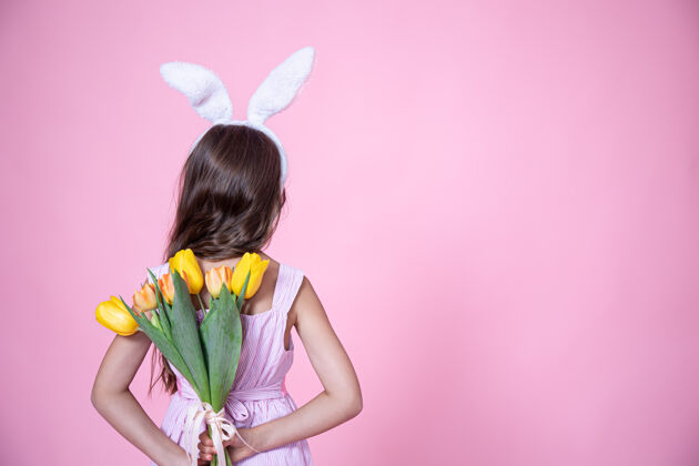 复活节一个有着复活节兔子耳朵的小女孩在一间粉红色的工作室里 手背上捧着一束郁金香耳朵郁金香兔子