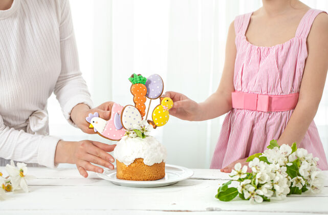 姜饼妈妈和女儿装饰着小蛋糕为家庭节日复活节做准备的理念女儿自制节日
