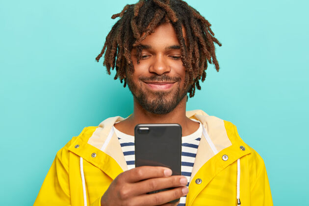 条纹皮肤黝黑的快乐男人 有恐惧 积极地看智能手机 看照片 穿黄色雨衣非洲裔男性设备
