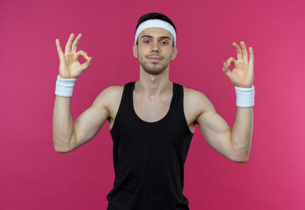 头带戴着头巾的年轻人微笑着做冥想姿势 手指站在粉红色的墙上男人运动手势