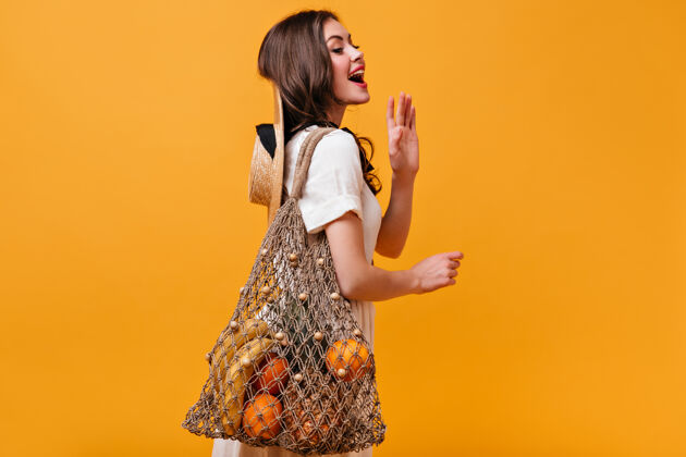 水果身着白色棉质连衣裙的迷人女子在橙色背景上摆出了一副串包的姿势女性化妆品连衣裙