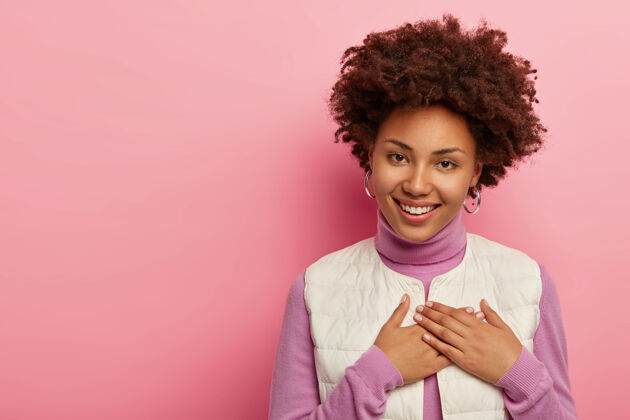 欣赏积极的非洲女人把手按在胸前 欣赏温暖的话语 微笑着轻轻地隔离在粉红色的墙上女性情感室内