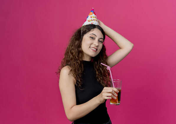 快乐一位年轻漂亮的女士 卷发 戴着节日帽 手里拿着鸡尾酒 开心而积极地笑着 生日派对的概念是粉色的派对粉色头发