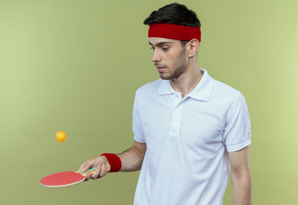 球拍戴着头巾 拿着乒乓球拍 站在绿墙上扔球的年轻人男人球运动