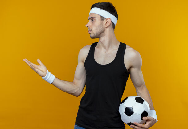 球戴着头巾的年轻运动型男子举着足球 站在橘色的墙上 伸出手臂向一边打听或争论足球抱着年轻