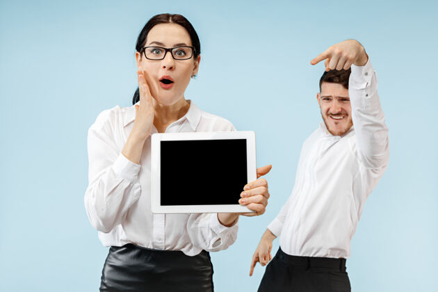 一起惊讶的商人和女人微笑在蓝色的墙上 并显示笔记本电脑或平板电脑的空屏幕小玩意商人打赌