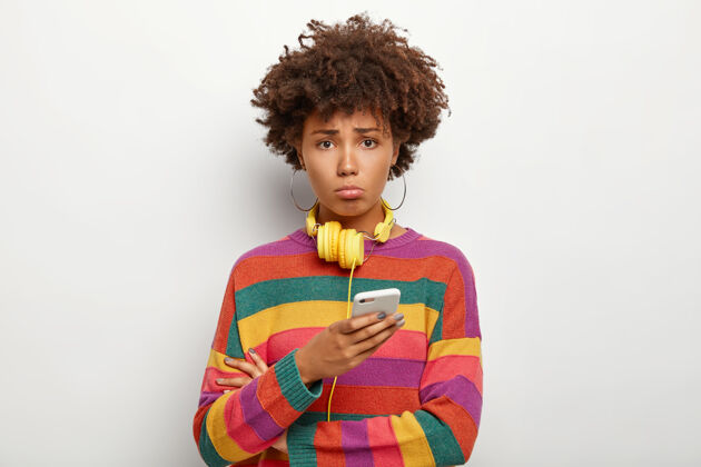 悲伤不满意的青少年卷发 使用智能手机 感到孤独和不安 穿着条纹毛衣不开心条纹毛衣