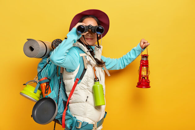 瓶子好奇的女背包客探索旅游目的地 用望远镜 穿着运动服 拿着煤油灯 背着背包携带旅游物品站徒步旅行女人