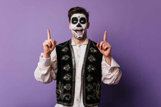 死亡之日一位身着墨西哥服装的高加索男士正在为派对做准备热情的男模在紫色的墙上摆出有趣的万圣节化妆姿势僵尸墨西哥死亡