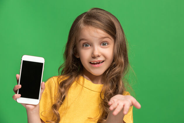 年轻快乐的少女站着 微笑着用手机在时尚的绿色工作室成功面部欢呼