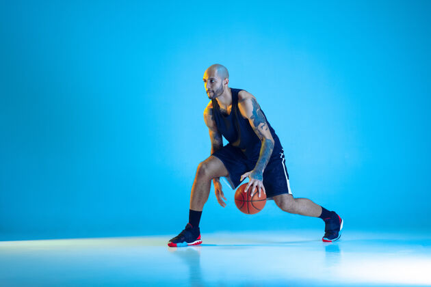 家伙年轻的篮球队员穿着运动服训练 在运动中练习 运动在霓虹灯下隔离在蓝色的墙上运动的概念 运动 活力和活力 健康的生活方式运动员活跃跳跃