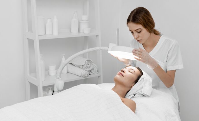 沙龙美容师为女性客户做美容常规女人灯治疗