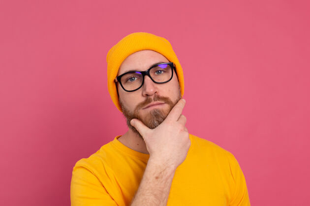 男性时尚帅气的留着胡子的欧洲男人的肖像 穿着休闲的黄色衬衫 戴着粉色背景的帽子和眼镜脸不刮胡子成功