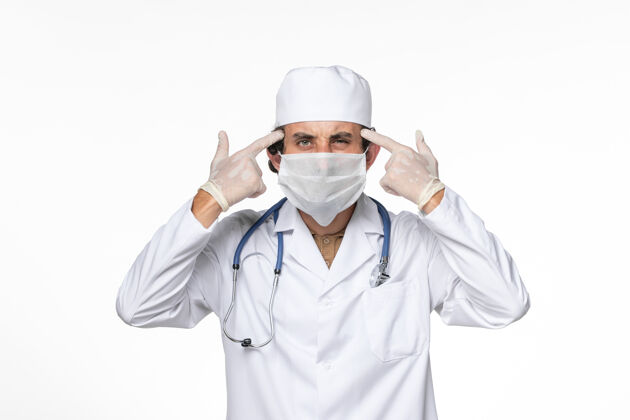 大流行正面图：男医生穿着医疗服 戴着口罩以防感染冠状病毒——关于白墙病毒喷溅冠状病毒大流行的思考面具西装外套