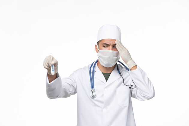 男性正面图：男医生穿着医疗服 戴着防冠状病毒口罩 白色办公桌上的手持装置病毒冠状病毒-疾病大流行持有外套疾病