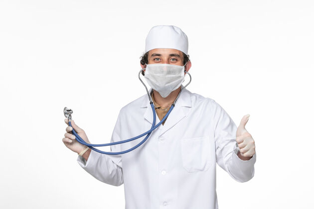 医生正面图：男医生穿着医疗服 戴着口罩 用听诊器在白墙飞溅的冠状病毒大流行中保护自己不受感染外套听诊器正面