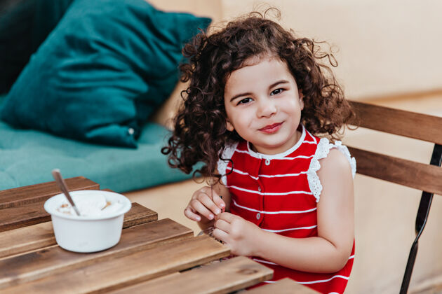 女儿黑眼睛的孩子在咖啡馆享受甜点时摆姿势微笑的小女孩吃冰淇淋的户外照片黑发冰淇淋餐馆