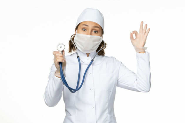 医生正面图女医生穿着白色的医疗服 戴着口罩 用听诊器在浅白的墙上做潘多米病毒病的药使用医疗病毒