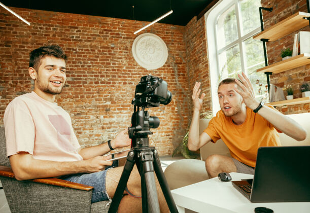视频日志两位年轻的白人男性博主穿着休闲服 用专业设备或摄像机在家里录制视频采访广播谈话男
