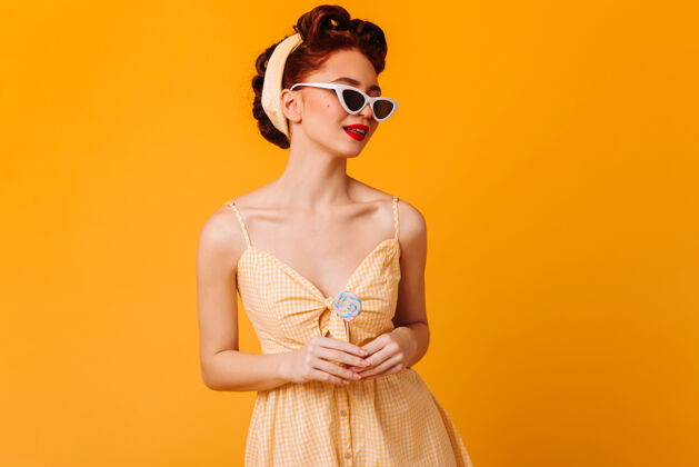 漂亮可爱的戴着太阳镜的女人黄色空间里姜汁女孩和棒棒糖的摄影棚照片发型表情性感