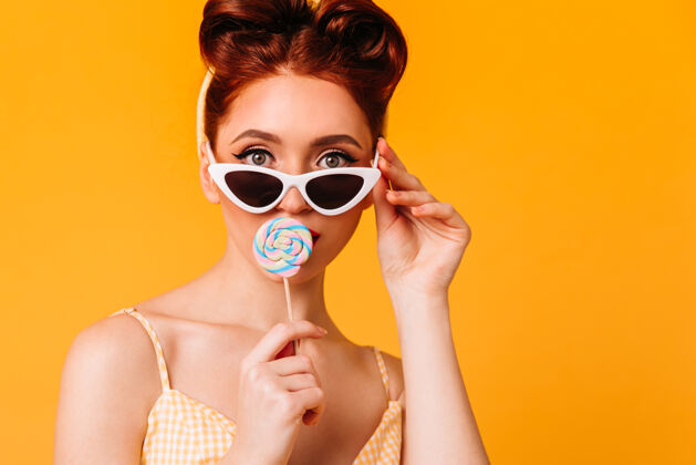 生姜漂亮的年轻女子正在舔硬糖戴着太阳镜的姜黄色小姑娘的正面图性感甜点时尚