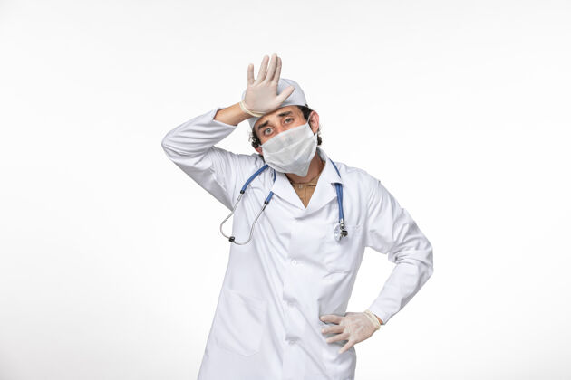 冠状病毒正面图：男医生穿着医疗服 戴着无菌口罩 以防冠状病毒在浅白的墙壁上飞溅 引起冠状病毒大流行专业查看防护